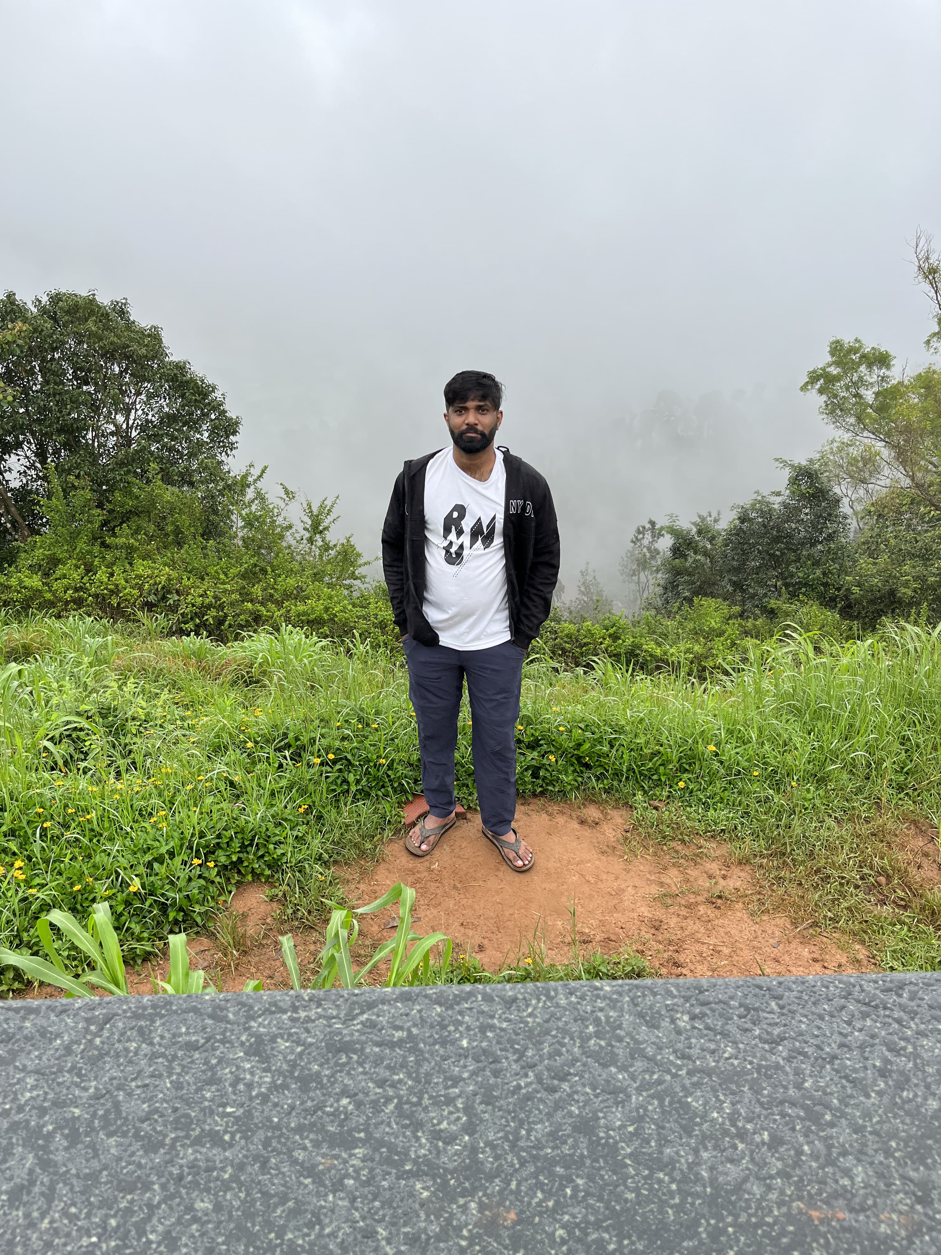 Anand standing in mist and green at a Coorg viewpoint.